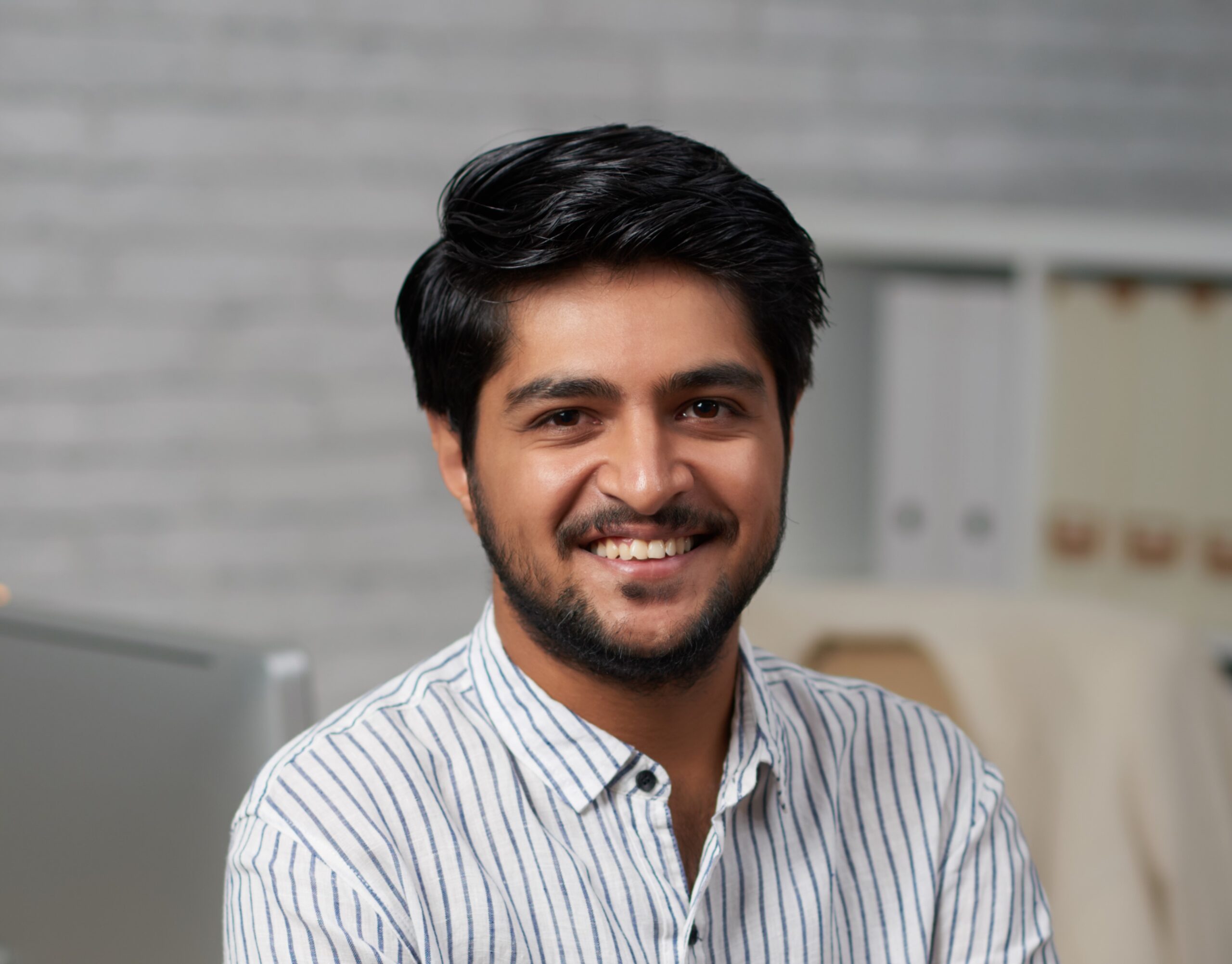 Confident young Indian businessman sitting on edge of his table and looking at camera